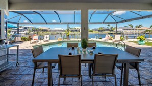 Uma área de refeições ao ar livre coberta, com piscina, cadeiras e uma mesa.