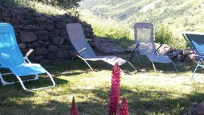 A garden with a stone wall, a blue chair, and a flower bed with pink flowers. - Chalet on the slopes in Valmeinier 1800 (Valmeinier)