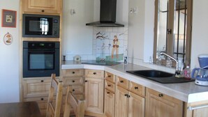 A kitchen with wooden cabinets, a microwave, an oven, a sink, and a window with a view. -  BASTIDON, POOL, 3000 M2 OF LAND, 2-4 PERS, APT, Luberon (Apt)