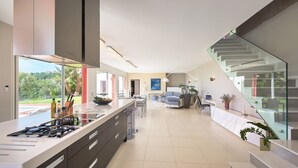 A modern kitchen with a large island, a dining area with a glass staircase, and a view of the outdoors. - SunlightProperties: SPLENDID: Villa, 4 Bedroom/ 3 bath, jacuzzi, heated pool (Peymeinade)