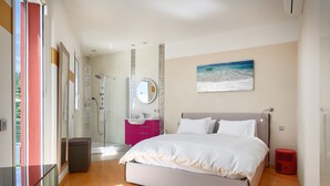 A modern bedroom with a large bed, a walk-in shower, and a painting of a beach scene. - SunlightProperties: SPLENDID: Villa, 4 Bedroom/ 3 bath, jacuzzi, heated pool (Peymeinade)