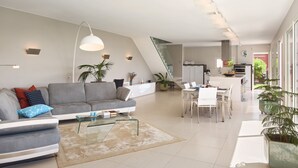 A modern living room with a grey sofa, a glass coffee table, and a dining area with a white table and chairs. - SunlightProperties: SPLENDID: Villa, 4 Bedroom/ 3 bath, jacuzzi, heated pool (Peymeinade)
