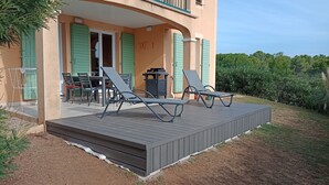 A covered outdoor area with two lounge chairs and a table, a covered patio with a table and chairs, and a building with green shutters and a butterfly decoration.