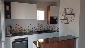 A modern kitchen with white cabinets, a black countertop, and a poppy flower backsplash.