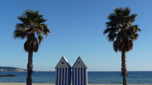 A beach scene with two striped beach huts and palm trees.