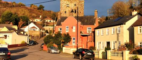 A street with residential buildings, a tower, and parked cars.