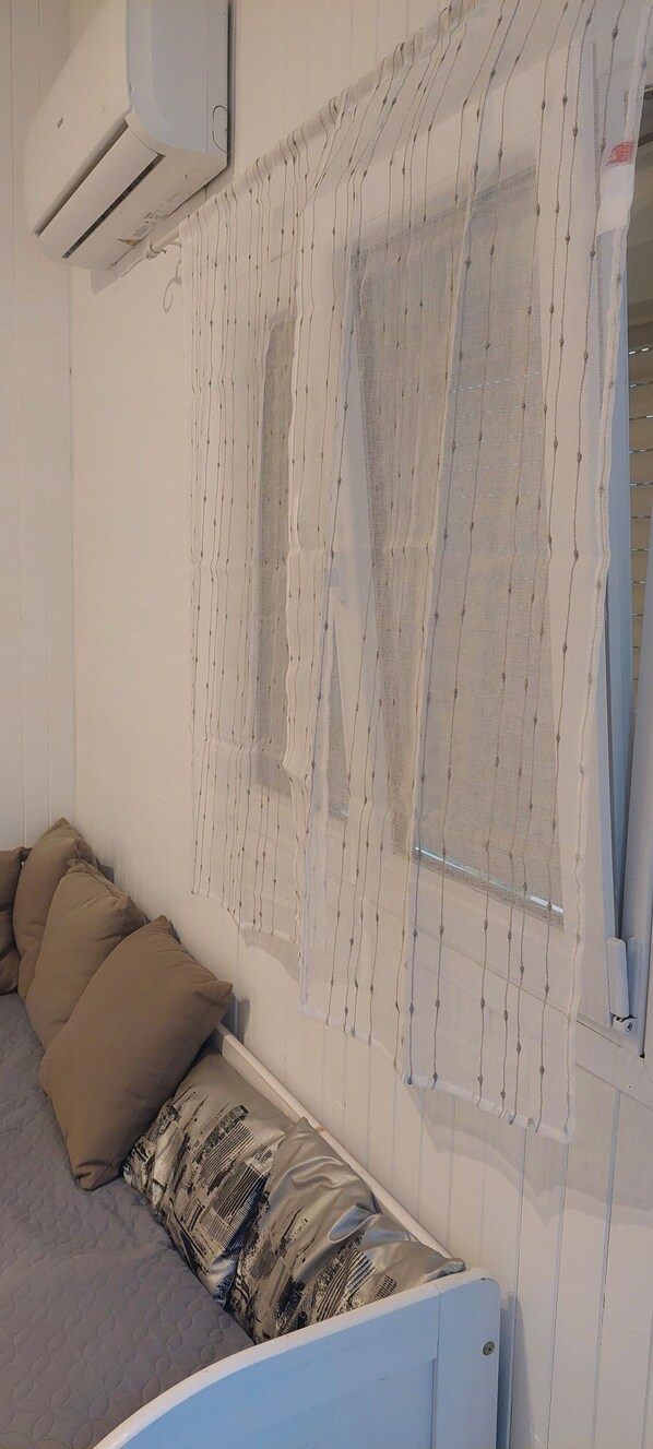A bedroom with a bed, pillows, a window with curtains, and an air conditioning unit. - If you like peace and quiet between sea and mountains (Zonza)
