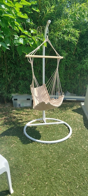 A white outdoor swing chair with a beige cushion, set on a grassy lawn with a bamboo backdrop.