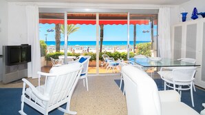 A balcony with a glass door leading to a beach view, white furniture, and a TV on the left. - UHC Piscis Apartments: Seafront Stay with Sea Views (Salou)