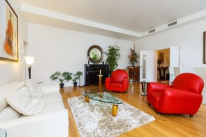 Un salon avec une table basse en verre, un fauteuil rouge, un canapé blanc et une petite table d’appoint.
