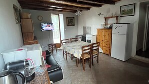A rustic kitchen with wooden beams, a dining table, chairs, a refrigerator, and a television.