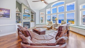 A spacious living room with a large leather sectional sofa, a fireplace, and a view of the ocean through large windows.