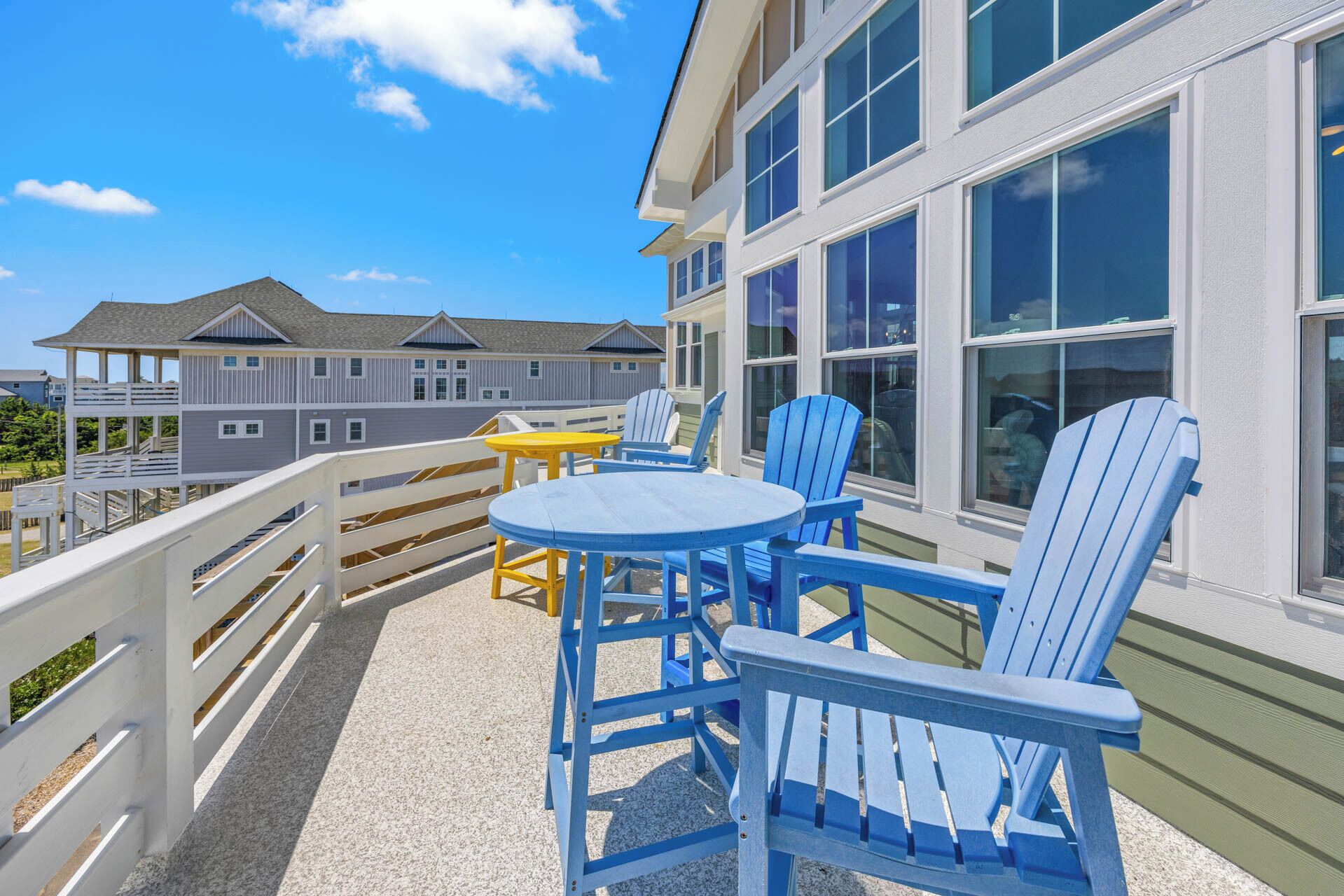 A balcony with blue Adirondack chairs, a small round table, and a yellow table.