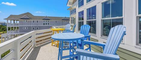 A balcony with blue Adirondack chairs, a small round table, and a yellow table.