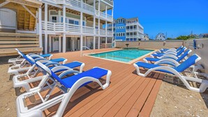 A cruise ship deck with a pool, sun loungers, and a multi-level building.