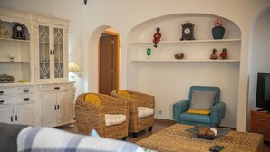 A living room with wicker furniture, a teal armchair, a white cabinet, and a television. - Villa 10 minutes from the beach, in a very quiet location w/ private pool (Armação de Pêra)