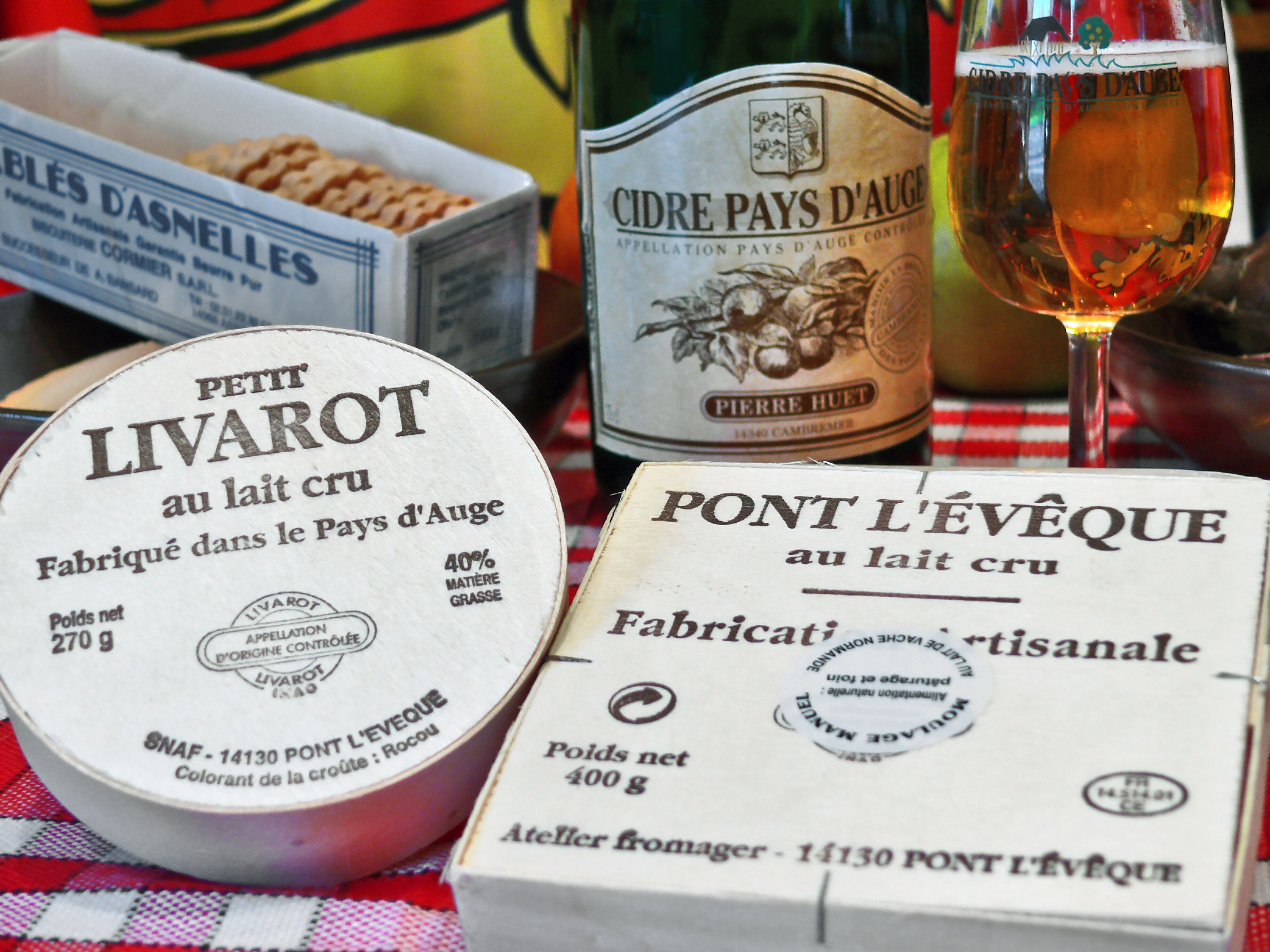 Ein Tisch mit verschiedenen Milchprodukten, darunter Livarot-Käse, Cidre Pays d'Auge und Pont L'Eveque-Käse.