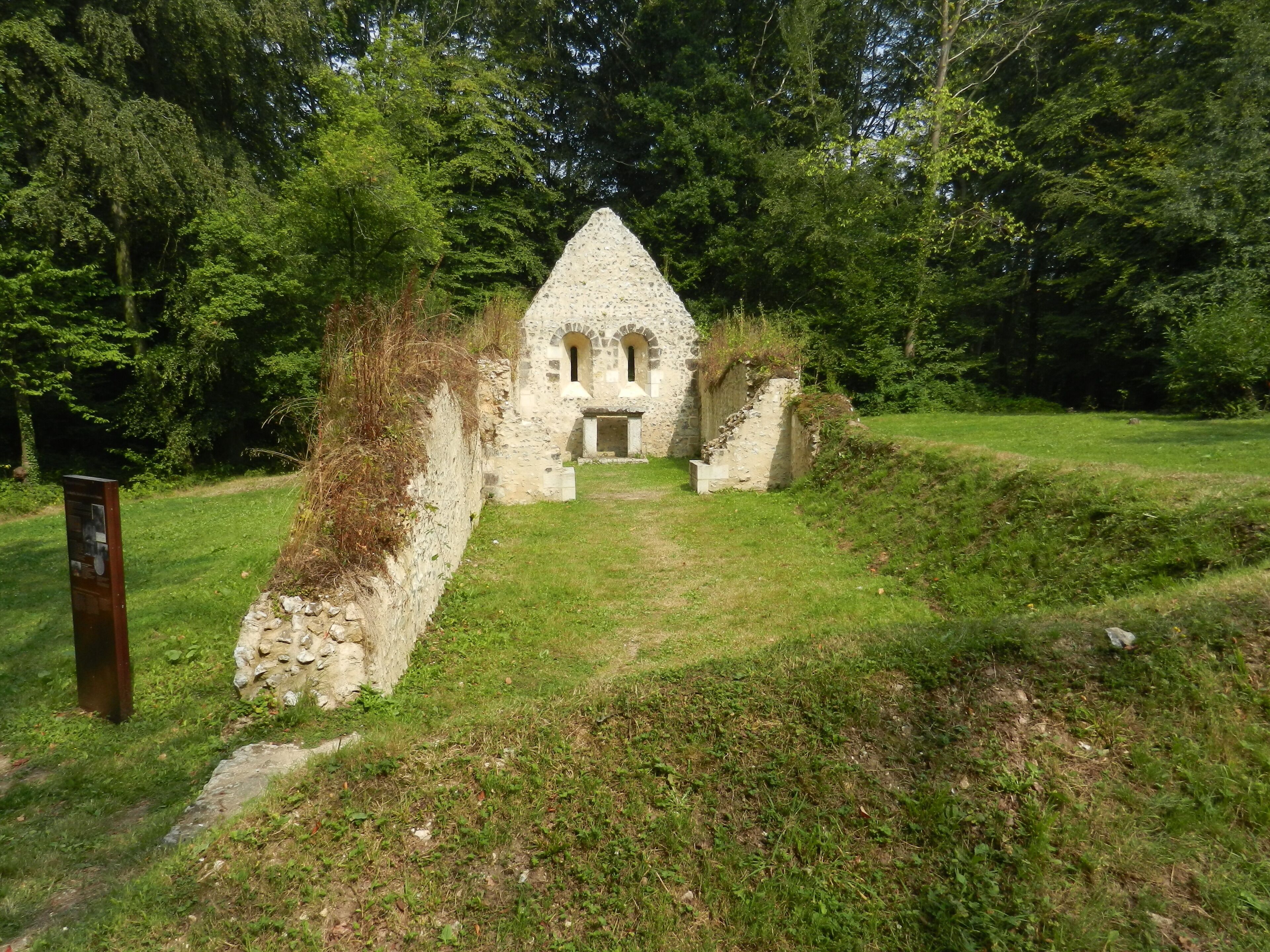 Un edificio in pietra con tetto a forma di triangolo e finestre ad arco, circondato da un prato e alberi.