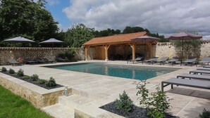 Ein Schwimmbecken mit Liegestühlen, einem hölzernen Pavillon und einer Steinmauer.