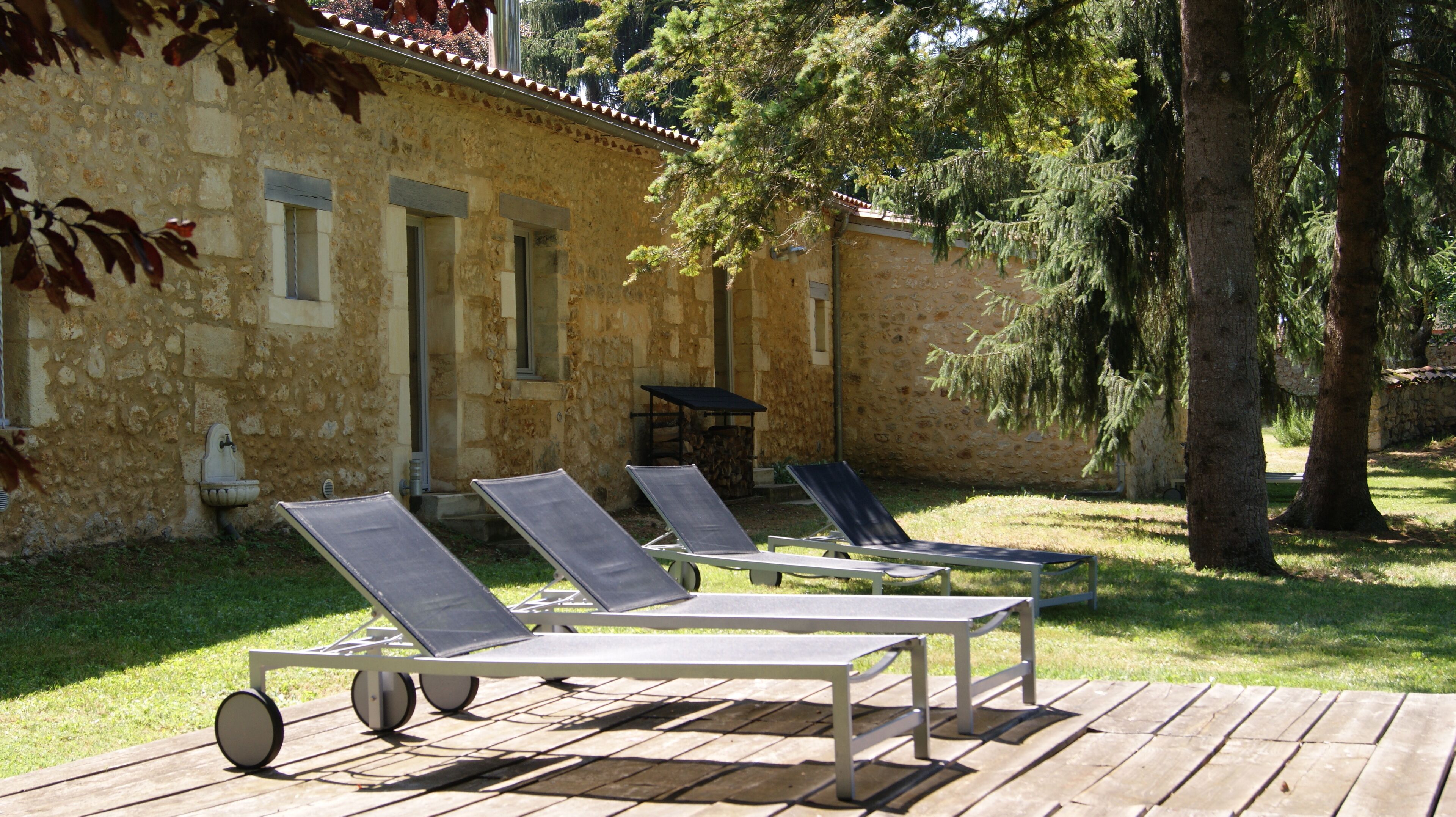 A stone building with a tiled roof, a wooden deck, and four sun loungers with wheels.