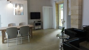 Ein geräumiger Wohnbereich mit einem Holzespeisetisch, Stühlen, einem Flachbildfernseher, einem kleinen Beistelltisch mit einer Vase und einer schwarzen Ledersofa.