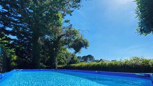 Una piscina azul cristalina rodeada de árboles y un seto.