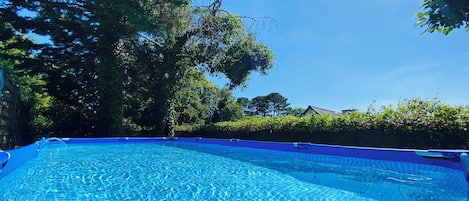 A clear blue swimming pool surrounded by trees and a hedge.
