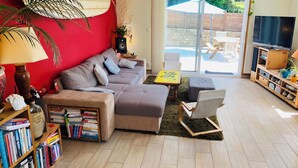 Una sala de estar con una pared roja, un sofá gris, una mesa de centro de madera y un televisor sobre un mueble de madera.