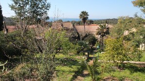 Un paysage rural caractérisé par des bâtiments aux toits de tuiles rouges, une végétation luxuriante et une vue dégagée sur la mer.