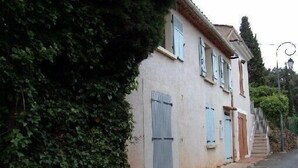 Un bâtiment à deux étages, doté d’une façade de couleur claire, de volets bleus et d’un escalier menant à l’étage supérieur.