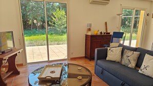 A living room with a blue sofa, a glass coffee table, and a TV on a wooden stand. - Le Verdon Sur Mer: House / Villa - Soulac / Le Verdon sur Mer (Le Verdon-sur-Mer)