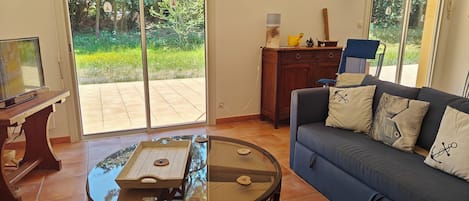 Un salon avec un canapé bleu, une table basse en verre et un téléviseur posé sur un meuble en bois.