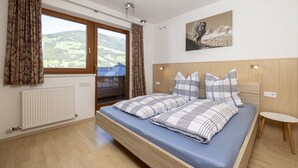 A bedroom with a bed, a window with curtains, a radiator, and a painting on the wall. - Large apartment: sunny, bright and quiet - modern - with a great view  (Ramsau im Zillertal)