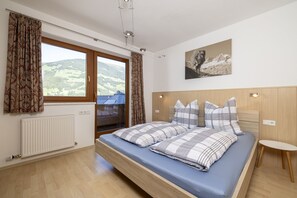 A bedroom with a bed, a window with curtains, a radiator, and a painting on the wall. - Large apartment: sunny, bright and quiet - modern - with a great view  (Ramsau im Zillertal)