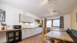 A modern kitchen with white cabinets, a wooden dining table, and a built-in bench. - Large apartment: sunny, bright and quiet - modern - with a great view  (Ramsau im Zillertal)