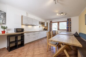 A modern kitchen with white cabinets, a wooden dining table, and a built-in bench. - Large apartment: sunny, bright and quiet - modern - with a great view  (Ramsau im Zillertal)