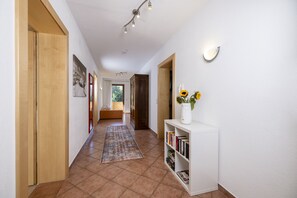 A hallway with a wooden door, a bookshelf with books, a vase with flowers, and a rug. - Large apartment: sunny, bright and quiet - modern - with a great view  (Ramsau im Zillertal)