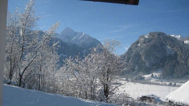A snowy mountain landscape with a wooden deck and a view of snow-covered trees and mountains. - Large apartment: sunny, bright and quiet - modern - with a great view  (Ramsau im Zillertal)