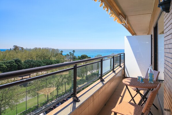 A balcony with a view of the sea, a table with a bottle and a cup, and a whiteboard.