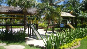 Un parc infantil amb tobogan i estructura per escalar, envoltat de palmeres i plantes tropicals.