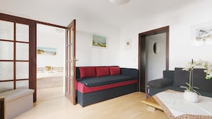 Uma sala de estar moderna com um sofá, uma mesinha com um vaso de flores e vista para um quarto através de uma porta de vidro.