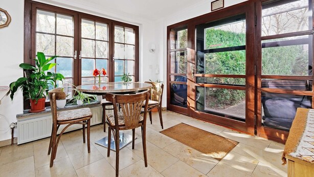 Uma sala de jantar com uma mesa redonda, quatro cadeiras de madeira e plantas em vasos.