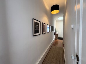 A hallway with framed text on the wall, a door on the right, and a light fixture above.