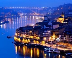 A waterfront cityscape at night with illuminated buildings and boats docked along the river. - Porto, City Center Apartment - Right in the Heart of the City! (Porto)
