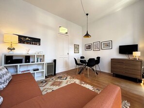 A modern living room with a sofa, a dining table with chairs, a TV, and a fireplace.