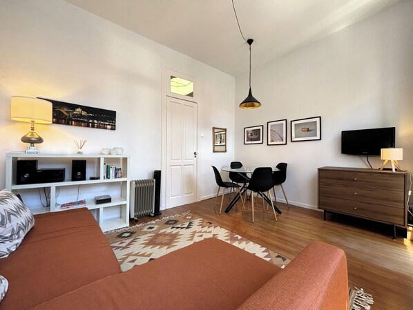 A modern living room with a sofa, a dining table with chairs, a TV, and a fireplace. - Porto, City Center Apartment - Right in the Heart of the City! (Porto)