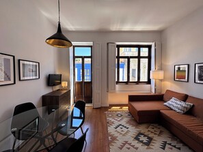 A modern living room with a glass dining table, a brown sofa, and a patterned rug. - Porto, City Center Apartment - Right in the Heart of the City! (Porto)
