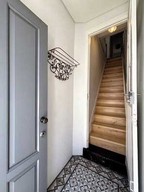 A hallway with a grey door, a black metal shelf, a wooden staircase, and patterned floor tiles. - Porto, City Center Apartment - Right in the Heart of the City! (Porto)