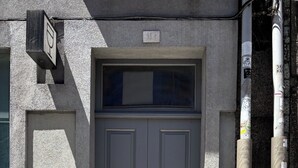 A gray double door with a small window above it, set in a textured wall.