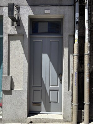 A gray double door with a small window above it, set in a textured wall. - Porto, City Center Apartment - Right in the Heart of the City! (Porto)